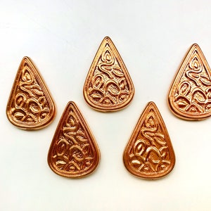 May include: Five gold-colored metal teardrop-shaped embellishments with an intricate design. Each teardrop has a raised, ornate pattern.