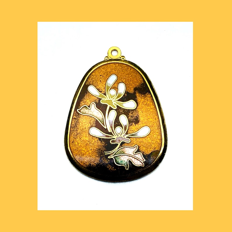 May include: A gold pendant with a brown and black enamel background and a white floral design.