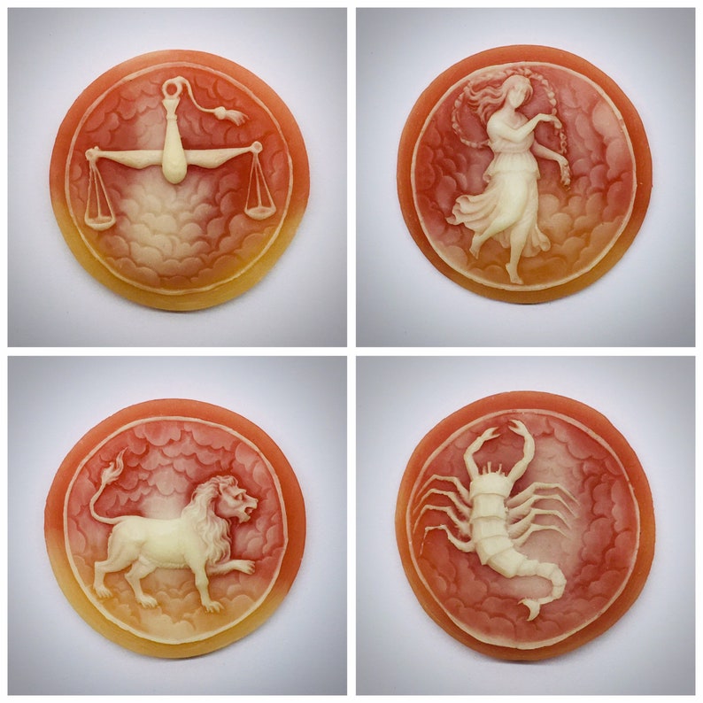 May include: Four round, red and white cameo-style pendants with different zodiac symbols. The symbols are Libra, Aquarius, Leo, and Scorpio.