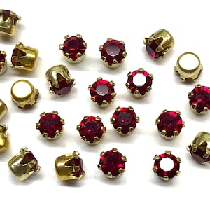 May include: A collection of red rhinestone embellishments with gold settings. The rhinestones are round and have a faceted design. The settings are claw-set and have a crown-like design.