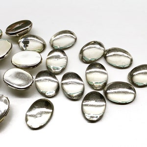 May include: A collection of oval-shaped, clear glass stones with a slightly iridescent finish. The stones are scattered on a white surface.