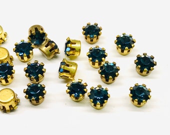 May include: A collection of 18 blue glass rhinestones with gold settings. The rhinestones are round and have a faceted design. The settings are round and have a crown-like design.