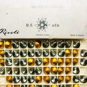 May include: A box of Rivoli Black Diamond brand rhinestones in gold and clear colors. The box is labeled "D.S. & Co. Trade Mark" and "Made in Austria".