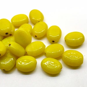 May include: A pile of yellow oval-shaped glass beads. The beads are smooth and glossy.