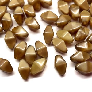 May include: A collection of light brown, geometric beads with a glossy finish. The beads have a unique shape, with a flat top and bottom and angled sides. They are scattered across a white surface.