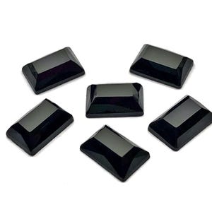 May include: Six rectangular, black gemstones with beveled edges are arranged on a white background. The gems have a glossy, polished appearance, reflecting light. These could be used for jewelry making or other crafts.