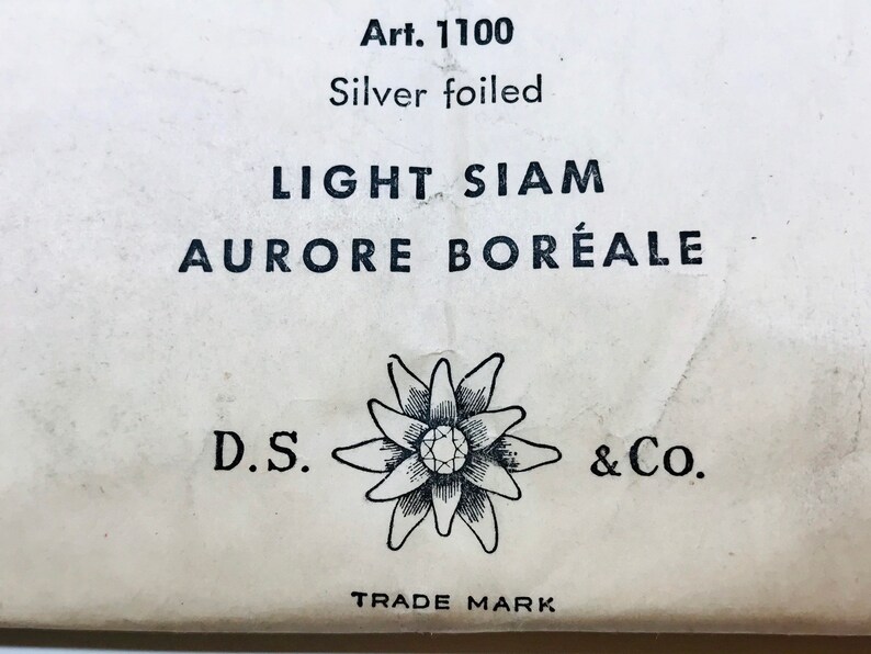 以下が含まれることがあります： 「Art. 1100 Silver foiled LIGHT SIAM AURORE BOR&Eacute;ALE」と黒文字で書かれた白いラベルと、中央にダイヤモンドがついた花の白黒イラスト。ラベルには「D.S. & Co. TRADE MARK」の文字も印刷されている。
