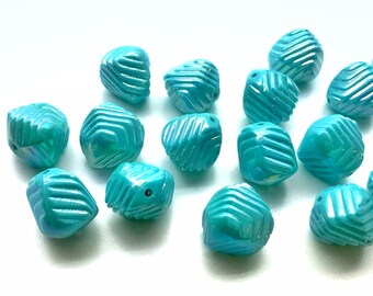 May include: A group of 13 turquoise blue iridescent glass beads with a faceted, geometric design. The beads are scattered on a white surface.