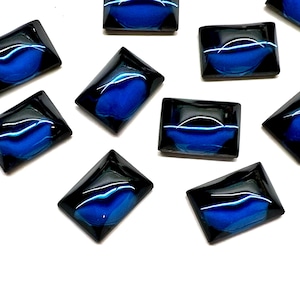 May include: A collection of rectangular cabochons featuring a deep blue center that transitions into black edges. Each piece has a smooth, polished, and reflective surface with a distinct light reflection visible across the top of the blue area.