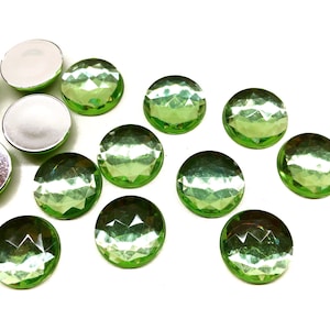 May include: A collection of 12 green, round, faceted, adhesive backed gems. The gems have a shiny, iridescent finish.
