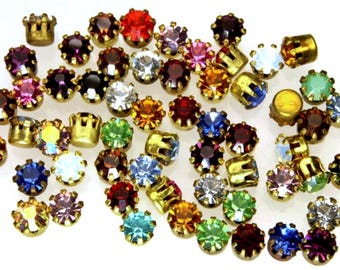 May include: Assortment of colorful, round, glass rhinestones with gold settings. The rhinestones are in various colors, including red, blue, green, yellow, and purple.