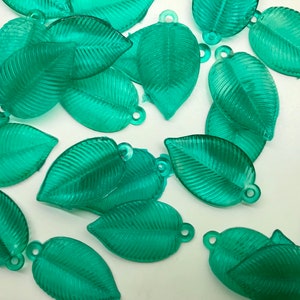 May include: A collection of green leaf-shaped charms with a textured surface. The charms have a hole at the top for attaching to jewelry or other crafts.