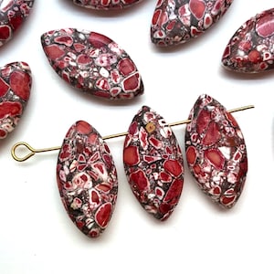 May include: Oval-shaped beads with a mosaic pattern of red, white, and dark gray. The beads are strung on a gold-colored wire, showcasing their unique, natural design. These beads are ideal for jewelry making.
