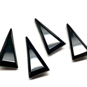 May include: Four black triangular shaped gemstone cabochons. The cabochons are faceted and have a polished finish.