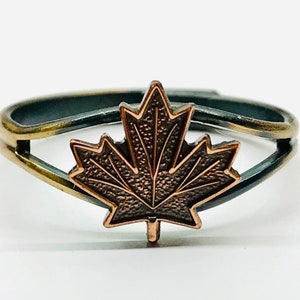 May include: A silver and gold adjustable ring with a copper maple leaf design.