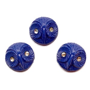 May include: Three cobalt blue owl-shaped buttons with a carved feather design. Each button features a silver-colored gem for eyes. The buttons are round and set against a white background.