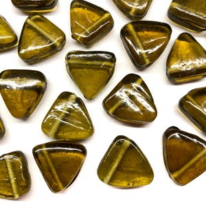 May include: A collection of triangular, amber-colored glass beads with a white stripe across the center. The beads are scattered on a white surface, showcasing their translucent quality and unique shape. These decorative beads are ideal for jewelry making or craft projects.