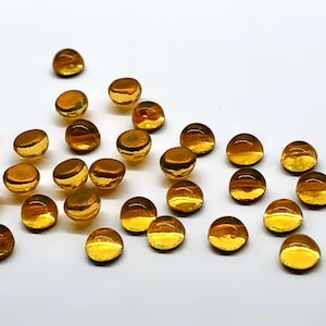May include: A group of small, round, golden glass beads. The beads are scattered on a white surface.