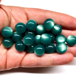 May include: A collection of teal green glass beads with a pearlescent finish. The beads are round and smooth, and they have a subtle shimmer.