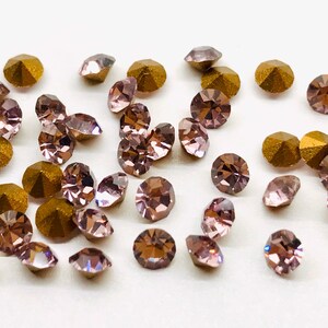 May include: A scattering of small, faceted, iridescent pink rhinestones and gold-toned rhinestones on a white background.
