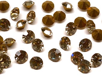 May include: A scattering of faceted, round and octagonal-shaped crystals in shades of brown and gold. The crystals are scattered across a white surface, catching the light and creating a sparkling effect. These could be used for jewelry making or other crafts.