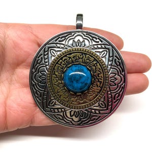 May include: A silver and gold pendant with a blue turquoise stone in the center. The pendant is round and has a detailed design.