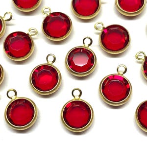 May include: A group of 15 red glass round charms with gold-colored metal loops. The charms are scattered on a white surface.