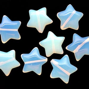 May include: Eight opalescent star-shaped beads with a light blue and white color scheme. The beads have a glossy finish and are arranged against a black background. These beads could be used for jewelry making or other craft projects.