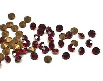 May include: A scattering of red and gold rhinestones on a white background. The rhinestones are small and round, with a faceted surface.