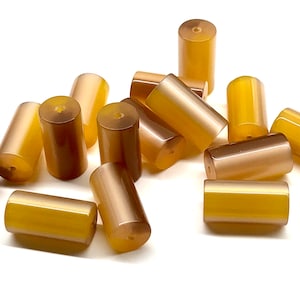 May include: A group of 13 smooth, polished, cylindrical beads in shades of brown and yellow. The beads are made of agate and have a natural, earthy look.