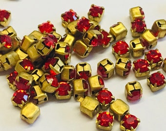 May include: A pile of red and gold metal embellishments. The embellishments are square shaped with a red jewel in the center.