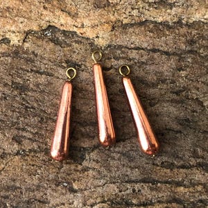 May include: Three copper-colored teardrop-shaped glass ornaments with gold-colored metal loops at the top.