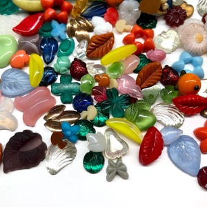 May include: Assortment of colorful glass and plastic beads in various shapes, including leaves, flowers, butterflies, and hearts. The beads are perfect for crafting and jewelry making.