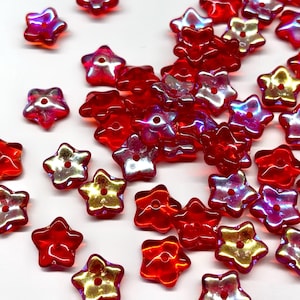 May include: A scattering of red star-shaped beads with iridescent centers. The beads have a hole in the center for stringing. The translucent beads reflect light, creating a shimmering effect. Ideal for jewelry making and crafts.