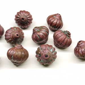 May include: A group of 12 copper-colored beads with a textured, ribbed design. The beads are round and have a small hole in the top for stringing.