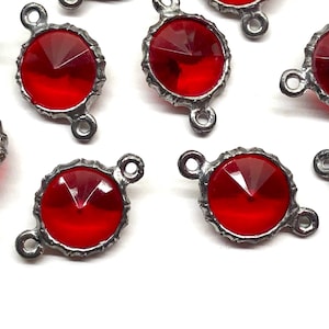 May include: Close-up of several red gemstone connectors with a faceted design. Each connector has a silver-colored metal frame and two loops for attaching to other components. The gemstones are a vibrant red color.