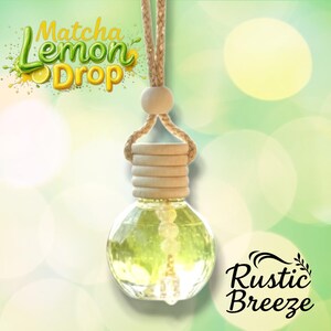 May include: A clear, round glass air freshener with a wooden cap and a woven rope for hanging. The liquid inside is light green. The words "Matcha Lemon Drop" and "Rustic Breeze" are displayed on the image.