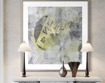 May include: A square framed wall art piece featuring an abstract composition of layered gray, charcoal, and pale yellow tones. The artwork includes faint, overlapping typographic elements and textured markings within a silver-toned frame.