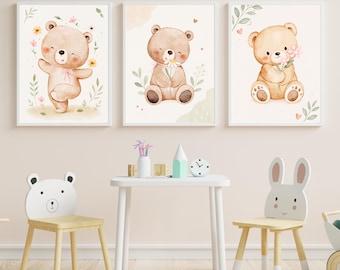 以下が含まれることがあります： 淡い茶色のテディベアを描いた水彩画風の額入りプリント3枚。左のクマは花の中に立ち、中央のクマはデイジーを持ち、右のクマはピンクの花束を持っています。これらのプリントは壁に飾られています。