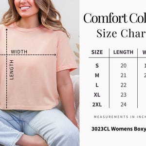 Puede incluir: Una camiseta de corte cuadrado color melocot&oacute;n con una tabla de tallas titulada Comfort Colors Size Chart. La tabla enumera las tallas de S a 2XL con medidas de largo y ancho en pulgadas. El texto 3023CL Womens Boxy Tee est&aacute; abajo.