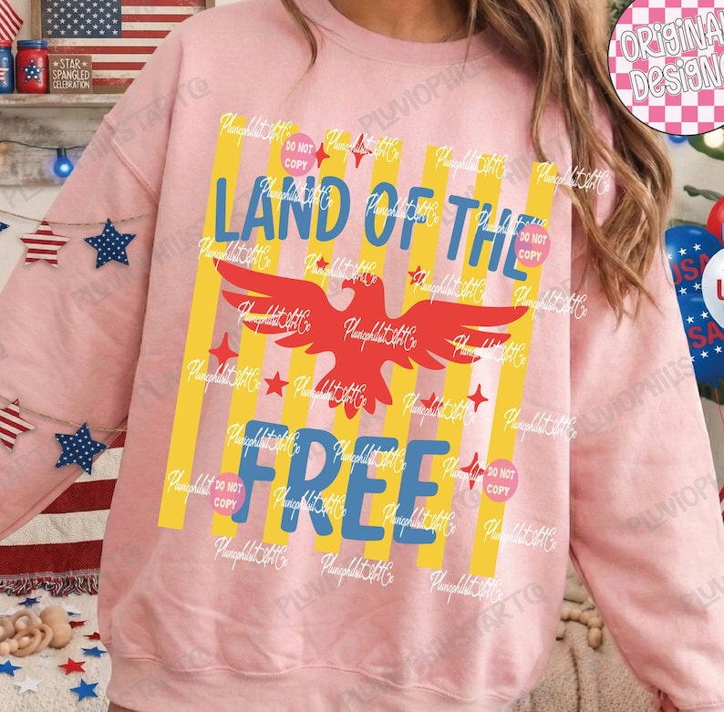 Puede incluir: Una sudadera rosa claro con un dise&ntilde;o patri&oacute;tico. El dise&ntilde;o presenta las palabras "LAND OF THE FREE" en azul, un &aacute;guila roja, rayas amarillas y estrellas rojas. La sudadera es de estilo c&oacute;modo e informal.