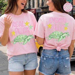 Puede incluir: Dos camisetas rosa claro con diseños a juego. Una dice "REAL QUICK" con un gráfico de tortuga y estrellas. La otra dice "EVENTUALLY" con un gráfico de tortuga y estrellas.