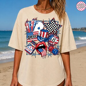May include: A beige t-shirt featuring a graphic design with patriotic elements. The design includes playing cards, a top hat, an 8-ball, dice, and the word "AMERICA". The design incorporates red, white, blue, and black colors.