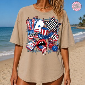 May include: Tan short-sleeved t-shirt with a patriotic graphic. The graphic includes playing cards, a top hat, an eight ball, dice, and a mouth with a flag-themed tongue. The word "AMERICA" is also featured.