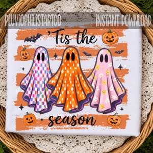 May include: A white graphic print featuring three ghosts over orange horizontal stripes. The ghosts have checkered, polka dot, and floral patterns. The text reads 'Tis the season' in black script, accompanied by small pumpkins, bats, and stars.