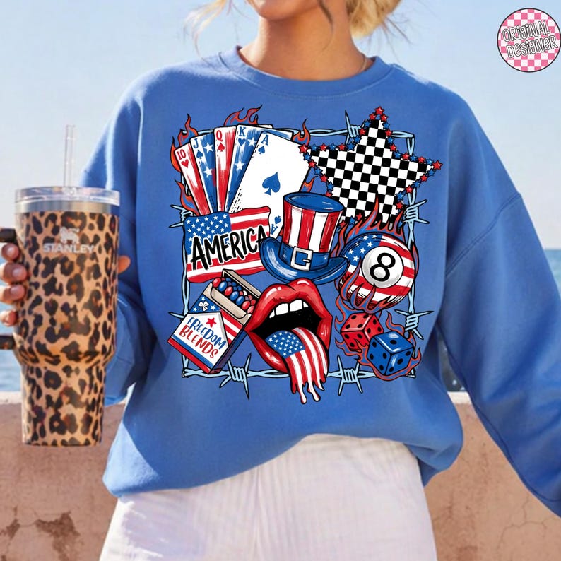 May include: A blue sweatshirt featuring a patriotic design with playing cards, a top hat, an eight ball, dice, and the word "AMERICA". The design incorporates red, white, and blue colors, with a barbed wire border.