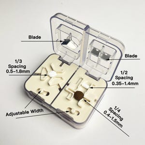 May include: A clear plastic pill cutter with a beige interior. The cutter has two compartments, each with a blade and adjustable spacing for different pill sizes. The spacing options are 1/3 (0.5-1.8mm), 1/2 (0.35-1.4mm), and 1/4 (0.4-1.5mm).