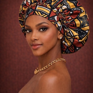 May include: A colorful, patterned bonnet in shades of red, yellow, and black. The bonnet is worn by a person with a gold chain necklace. The background is a solid, dark red.