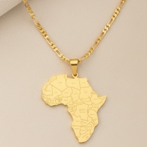 Può includere: Una collana color oro con un ciondolo a forma di continente africano. Il ciondolo presenta i contorni dettagliati dei paesi. La catena è una catena a maglia battuta color oro. La collana è presentata su uno sfondo neutro.