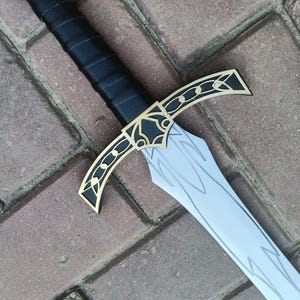 May include: A decorative sword with a black handle and a silver blade. The hilt features gold and black accents, and the pommel is adorned with a red gem. The blade has etched designs.